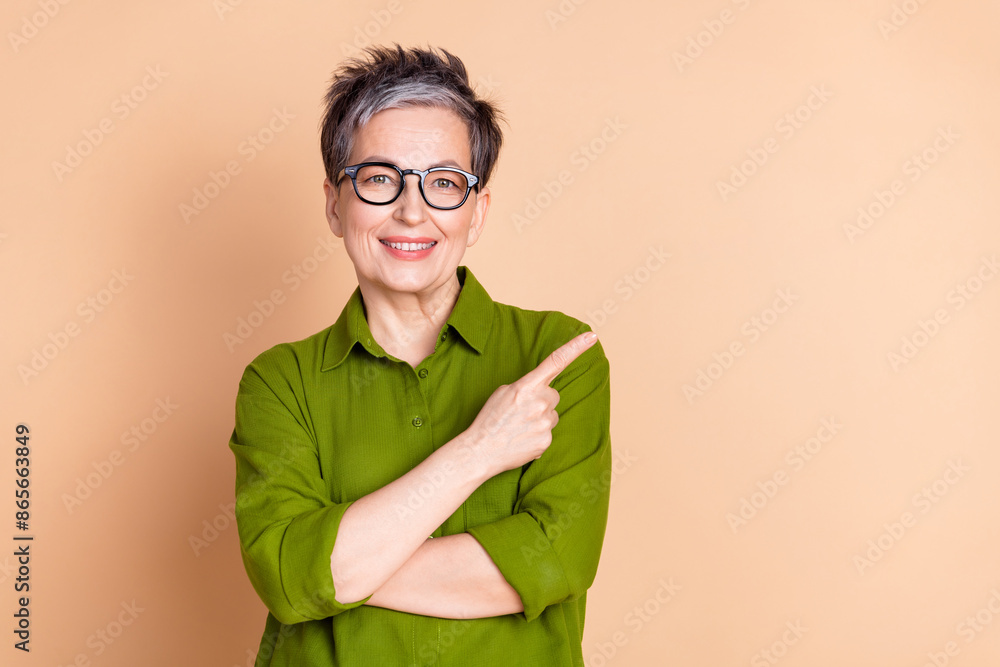 Photo portrait of attractive retired woman point empty space dressed stylish green clothes isolated on beige color background Photo portrait of attractive retired woman point empty space dressed stylish green clothes isolated on beige color background