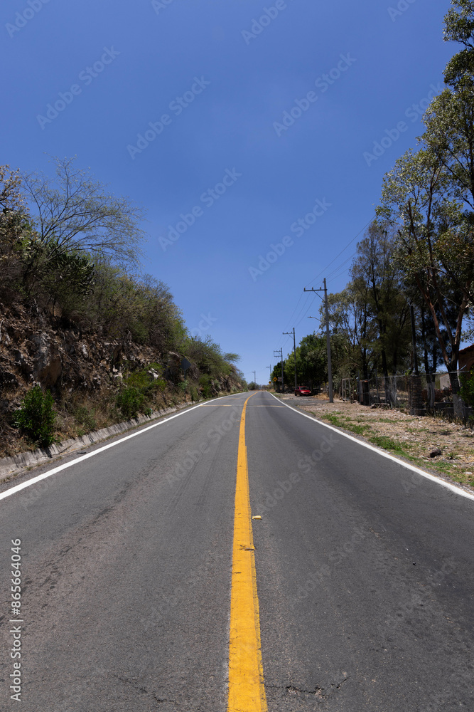 road in the middle of the hill with trees on each side, and a natural stone wall on one side with a completely blue sky road in the middle of the hill with trees on each side, and a natural stone wall on one side with a completely blue sky