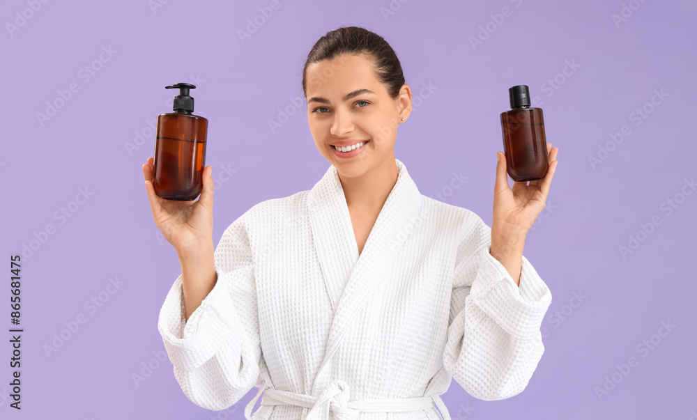 Beautiful young happy woman in bathrobe with bottles of cosmetic products on purple background Beautiful young happy woman in bathrobe with bottles of cosmetic products on purple background