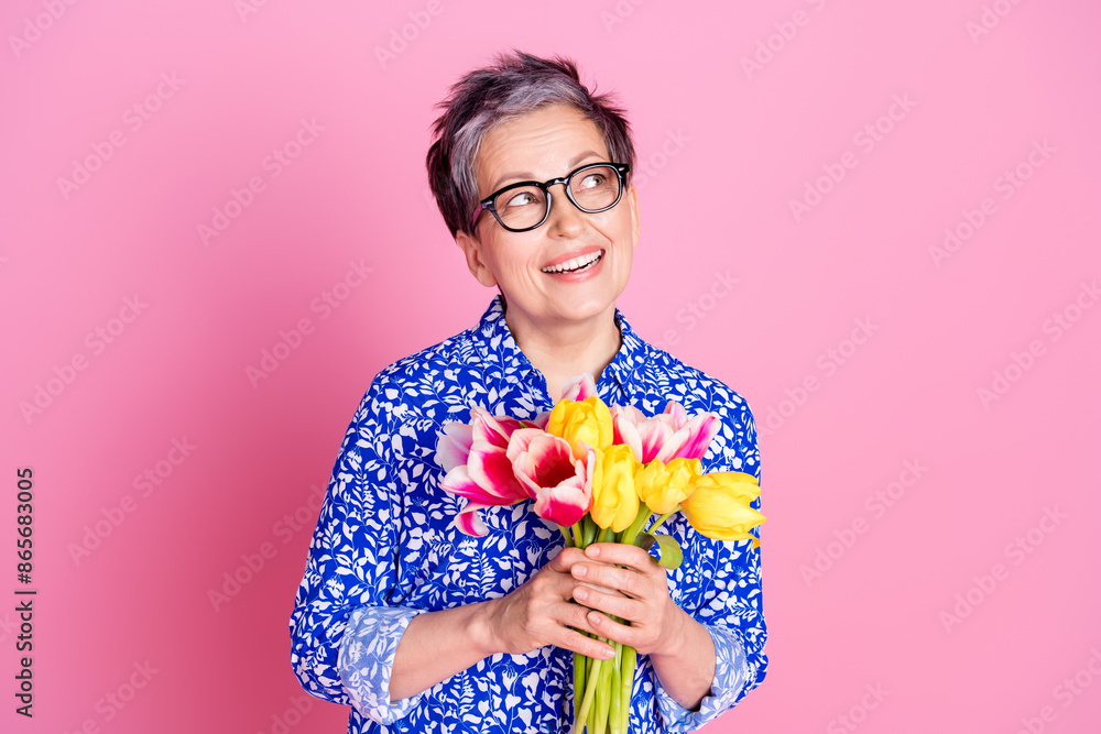 Photo of nice person with white gray hairstyle dressed print blouse hold tulips look at sale empty space isolated on pink color background Photo of nice person with white gray hairstyle dressed print blouse hold tulips look at sale empty space isolated on pink color background