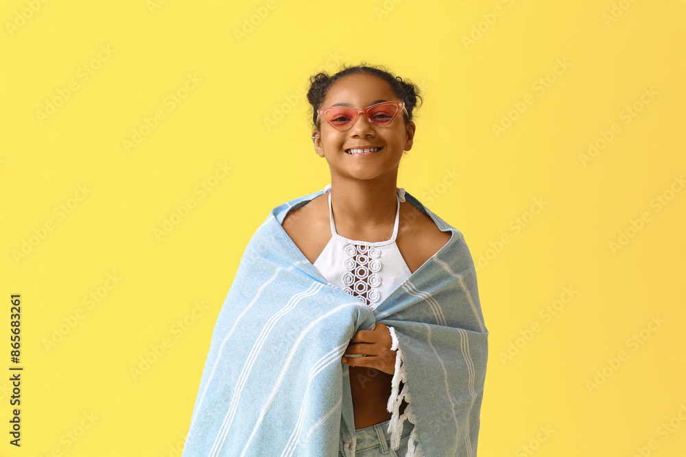 Happy African-American girl with beach blanket and flippers on yellow background Happy African-American girl with beach blanket and flippers on yellow background