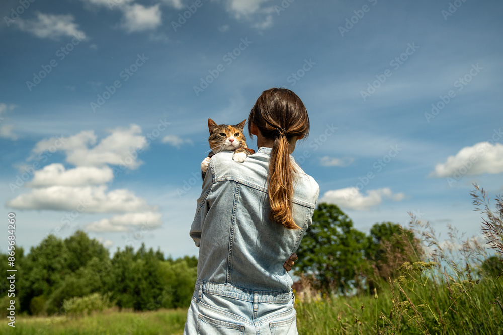 Domestic cat on leash walking outside for the first time, sitting on shoulder of loving woman owner, interested in new smells, worried and afraid, looking around. Walk with pets in nature. Domestic cat on leash walking outside for the first time, sitting on shoulder of loving woman owner, interested in new smells, worried and afraid, looking around. Walk with pets in nature.