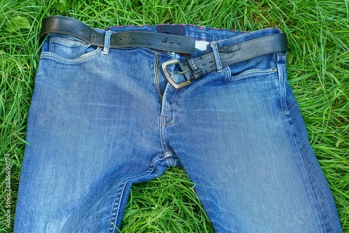 blue stylish fashionable men's jeans with an unzipped zipper and a black leather belt with an iron buckle lie on the green grass during the day outdoors photo