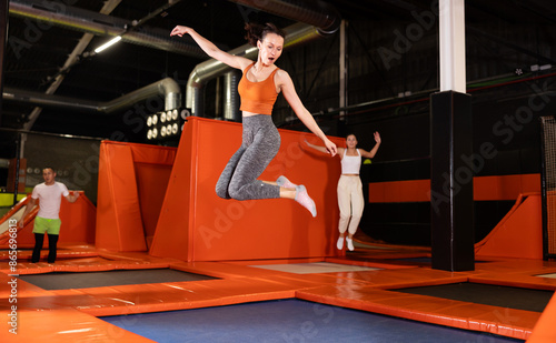Excited active woman enjoying moment of freedom and fun while jumping at well-equipped indoor trampoline arena..