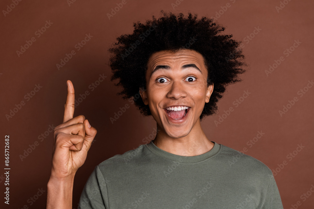 Portrait photo of young funky guy with curly haircut wearing gray t shirt surprised found idea pointing up isolated on brown color background Portrait photo of young funky guy with curly haircut wearing gray t shirt surprised found idea pointing up isolated on brown color background