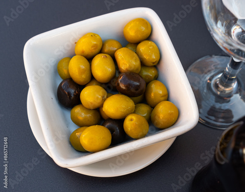 Square white bowl of mixed green and black pickled olives, popular snack often enjoyed with wine in Mediterranean and European cuisines photo