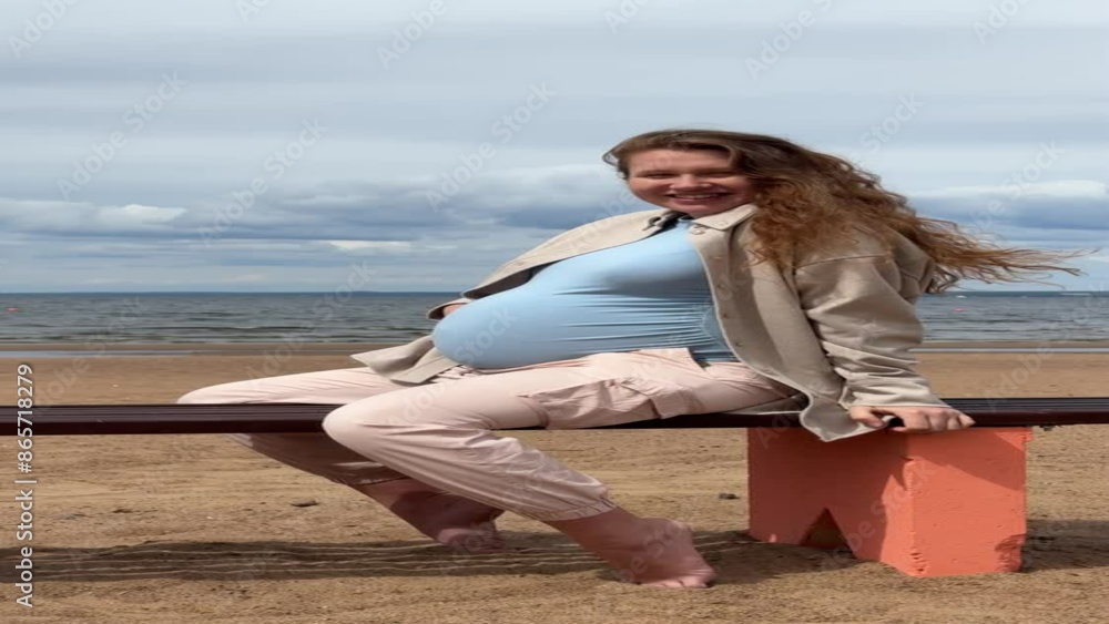 Young pregnant happy woman sitting on bench at the beach, sea and stroking her big belly Young pregnant happy woman sitting on bench at the beach, sea and stroking her big belly