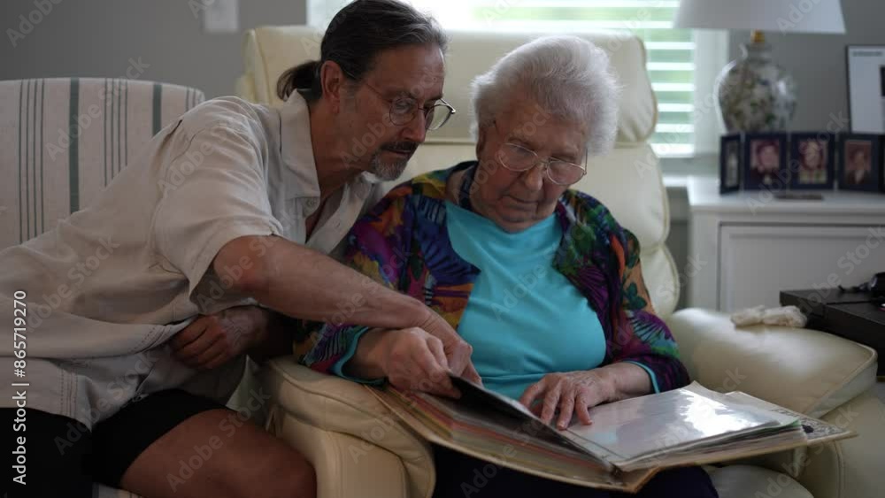 Smiling mature man looks at photo album of family memories with elderly mother. Smiling mature man looks at photo album of family memories with elderly mother.