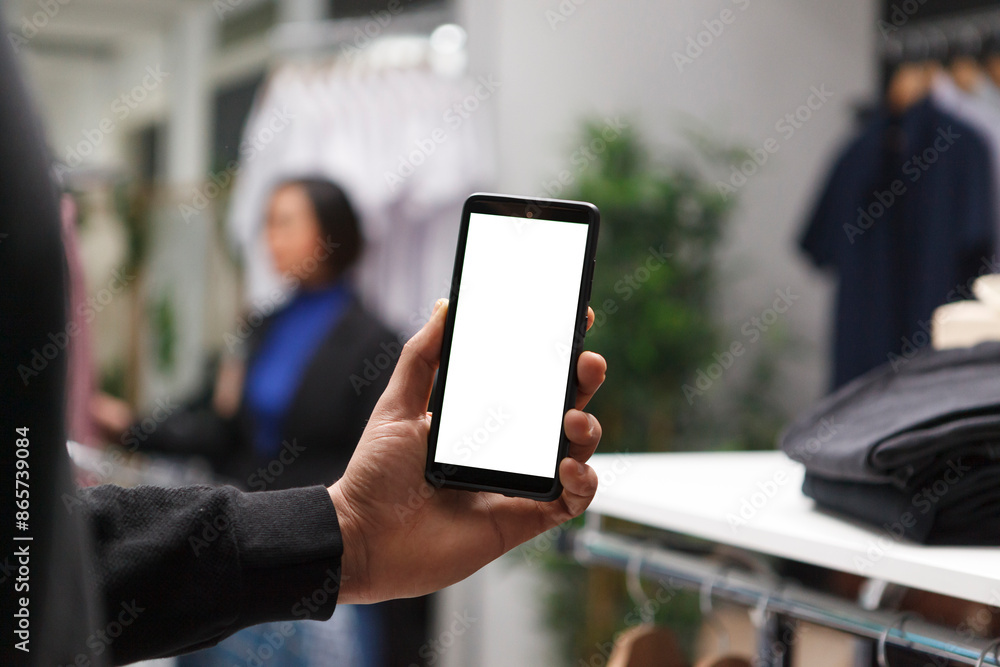 Shopping mall buyer hand holding smartphone with empty screen, browsing apparel online and in boutique. Clothing store customer using mobile phone with blank touchscreen mockup for promotion Shopping mall buyer hand holding smartphone with empty screen, browsing apparel online and in boutique. Clothing store customer using mobile phone with blank touchscreen mockup for promotion