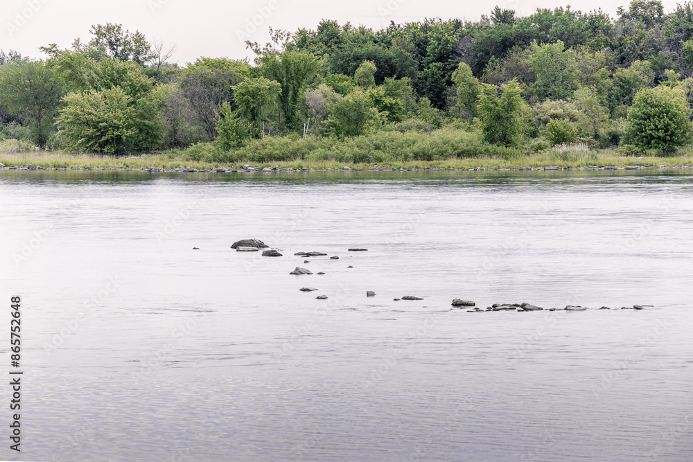A scenic lake shoreline with rocky terrain and trees in the background A scenic lake shoreline with rocky terrain and trees in the background