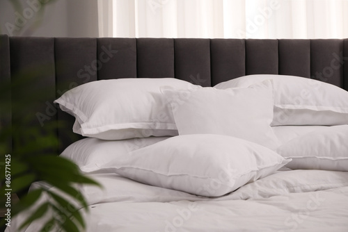 Many soft white pillows and duvet on bed indoors