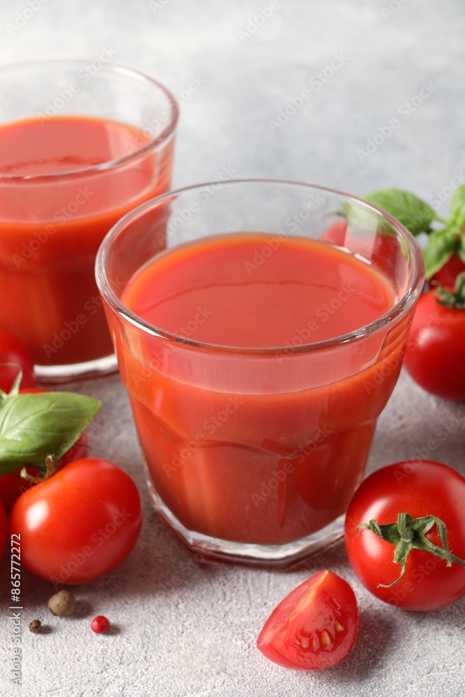 Tasty tomato juice in glasses, basil leaves, fresh vegetables and peppercorns on light grey table Tasty tomato juice in glasses, basil leaves, fresh vegetables and peppercorns on light grey table