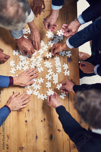 Above, hands and business people with puzzle in table for problem solving, teamwork and strategy. Employees, partnership and collaboration for innovation or solution with team building and support