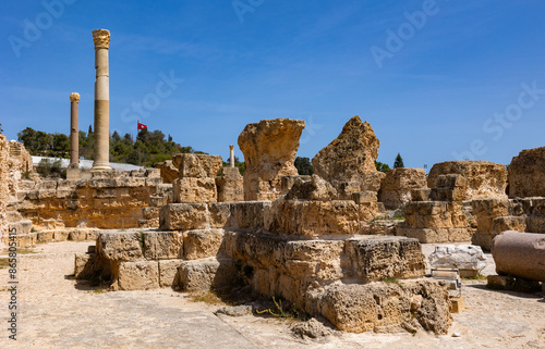 фотографія Scenic view of ruins of Roman Baths of Antoninus at Tunisian archaeological site of Carthage, featuring remnants of tall Corinthian columns and stone structures under blue sky