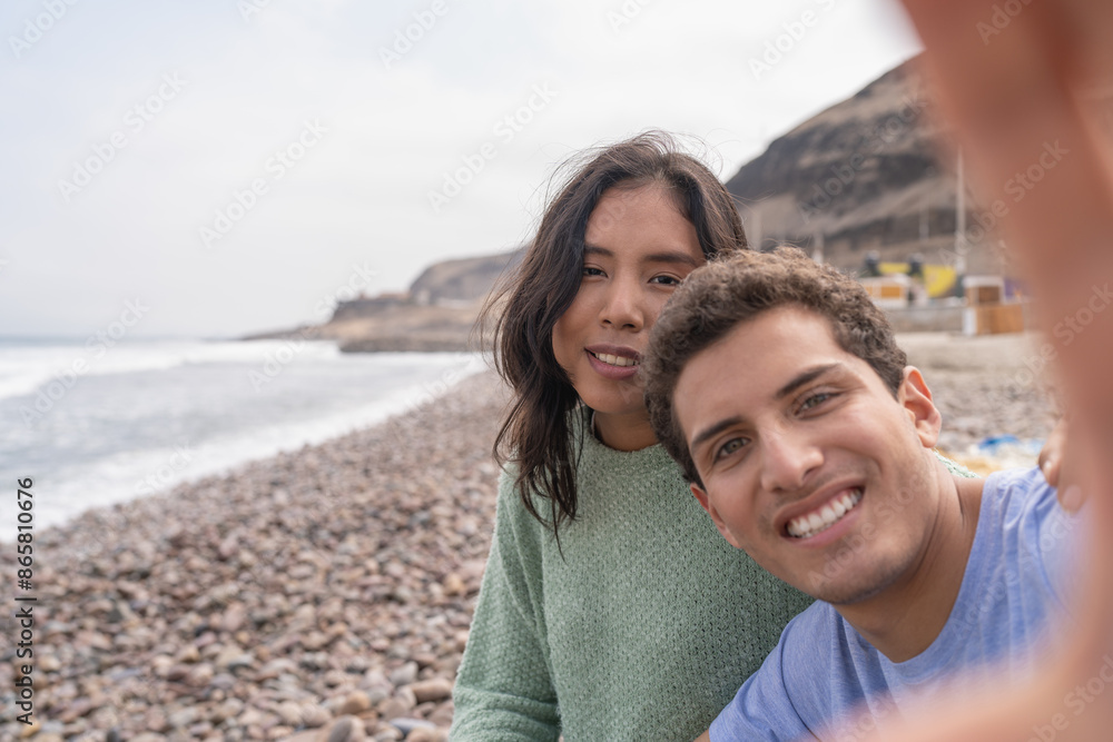 Latin young couple taking a selfie sitting on a beach Latin young couple taking a selfie sitting on a beach