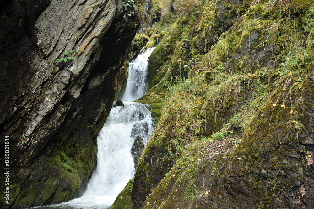 A small waterfall flows from the mountains through a narrow cleft in the mountains on a cloudy autumn day. A small waterfall flows from the mountains through a narrow cleft in the mountains on a cloudy autumn day.
