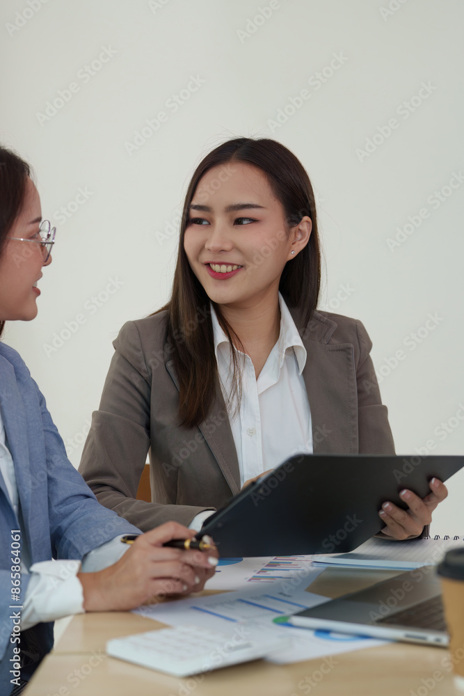 Two businesswomen discussing documents in an office, concept of teamwork and collaboration Two businesswomen discussing documents in an office, concept of teamwork and collaboration