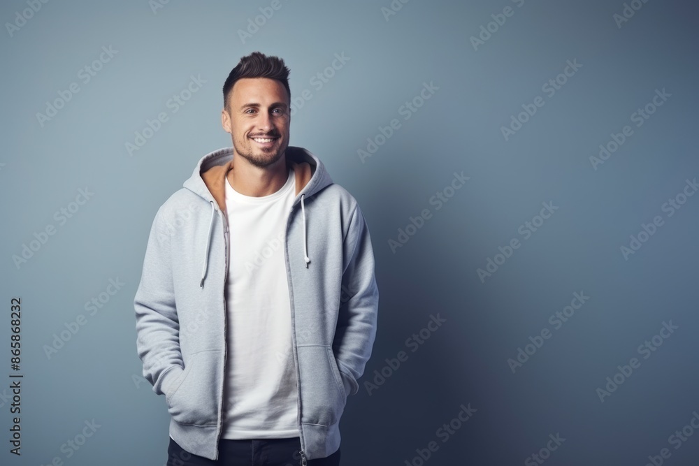 Obraz premium Portrait of a handsome young man wearing a hoodie and smiling while standing against grey background