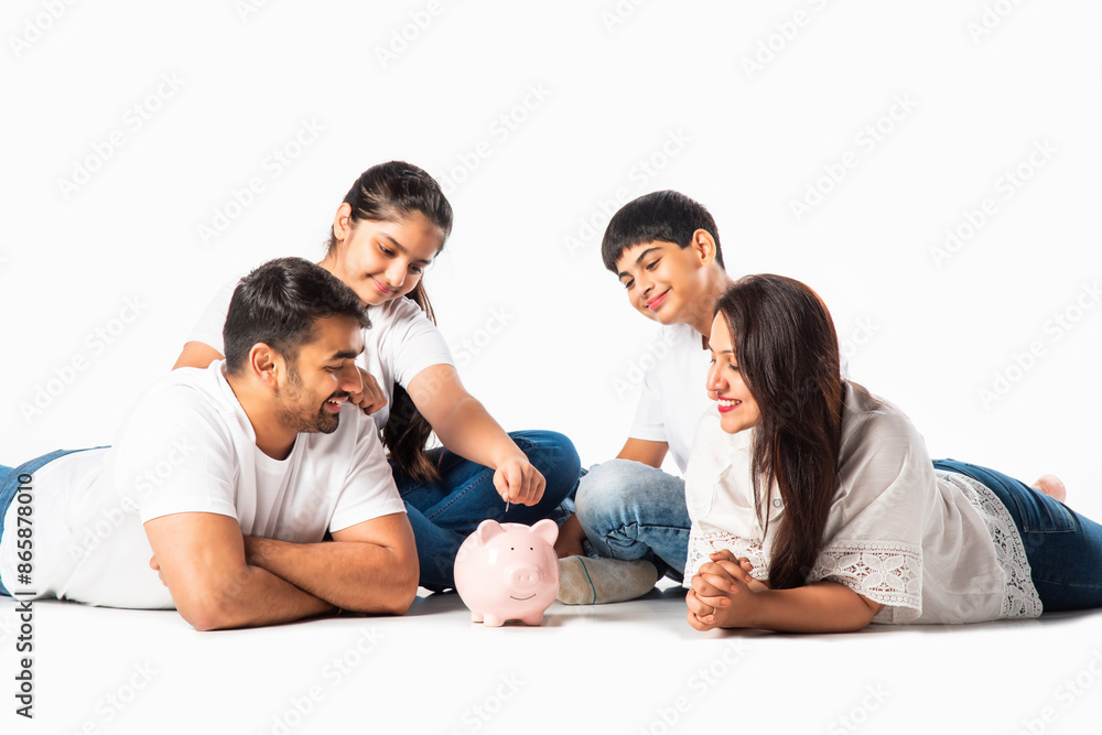Indian asian young parents family with two kids saving or putting money in piggy bank lying on floor Indian asian young parents family with two kids saving or putting money in piggy bank lying on floor