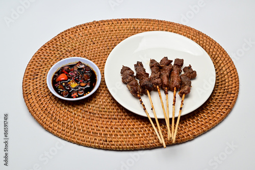 Satay with peanut sauce and soy sauce topped with chili slices and shallots is an Indonesian delight. Juicy grilled meat skewers paired with rich, spicy, and savory sauces