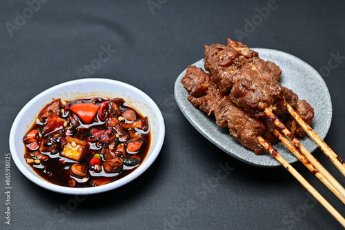 Satay with peanut sauce and soy sauce topped with chili slices and shallots is an Indonesian delight. Juicy grilled meat skewers paired with rich, spicy, and savory sauces