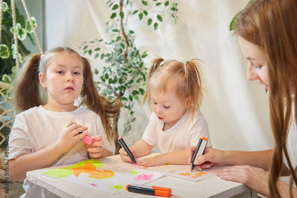 Young mother or babysitter, little daughter, sister teenager girl drawing at table in room. Painting, doing homework, family enjoying leisure at home Young mother or babysitter, little daughter, sister teenager girl drawing at table in room. Painting, doing homework, family enjoying leisure at home