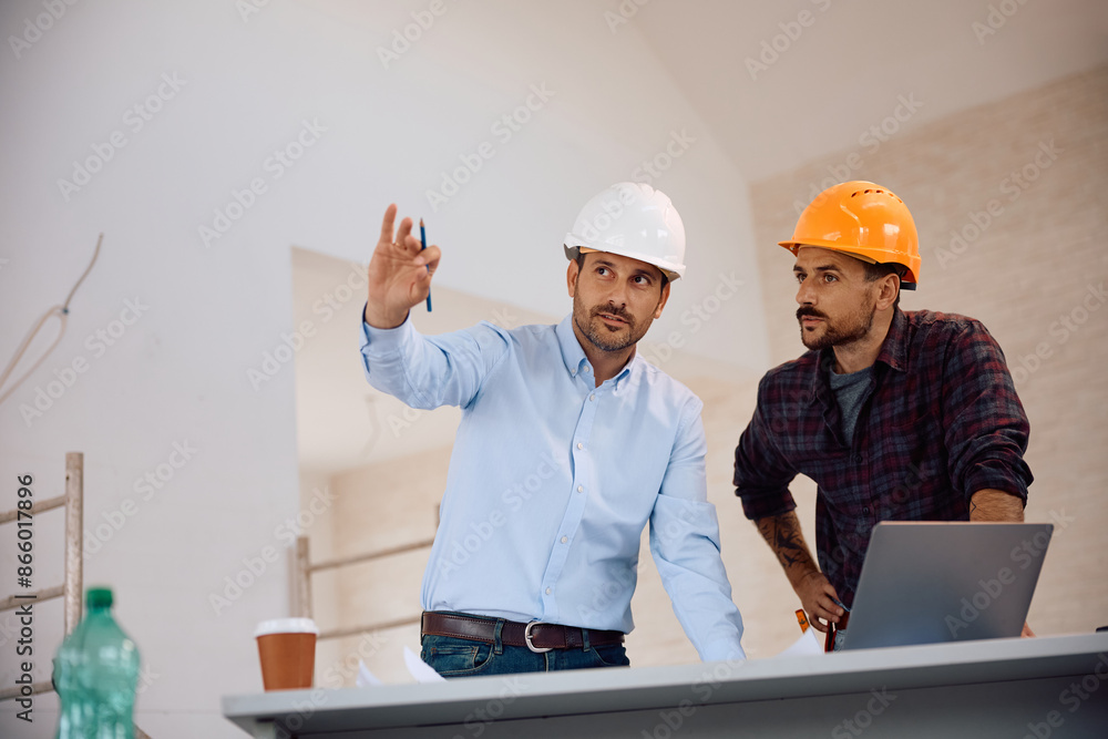 Building contractor and worker analyzing housing plans at construction site. Building contractor and worker analyzing housing plans at construction site.