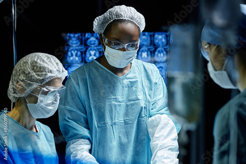 Waist up portrait of African American woman assisting in operation at hospital wearing mask and full protective clothing copy space