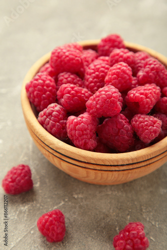 Raspberries in wooden bowl on grey concrete background