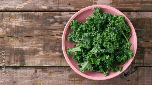 Artistic arrangement of organic kale leaves in a stylish pink bowl, enhancing the natural appeal of a wooden surface photo