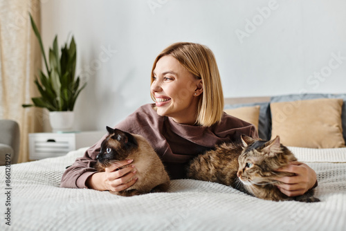 A woman with short hair relaxes on a bed with two cats by her side, enjoying a peaceful moment at home.