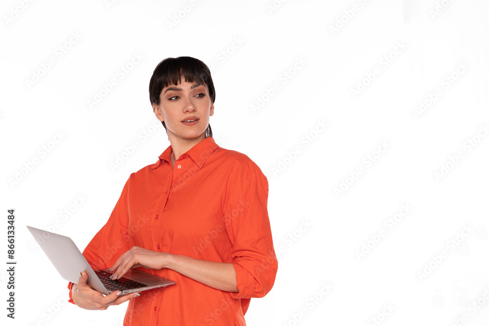 Young Woman in Orange Shirt Holding Laptop and Looking Away in Studio Young Woman in Orange Shirt Holding Laptop and Looking Away in Studio