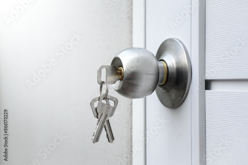 Keys and silver knob on a white wooden door against against the gray concrete background for forgot to close the door or lost the key and safety with security concept.