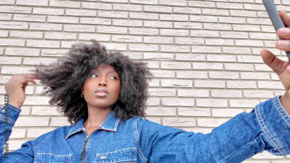 Young woman standing by a brick wall, taking selfies with her smartphone. Denim outfit, casual look. Young woman standing by a brick wall, taking selfies with her smartphone. Denim outfit, casual look.
