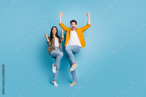 Full body portrait of two young people rejoice raise fists wear shirt isolated on blue color background