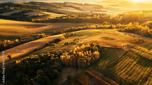 This aerial photograph captures a sprawling golden landscape with fields and rolling hills during an autumn sunset, highlighting the natural beauty and tranquility of rural life. photo