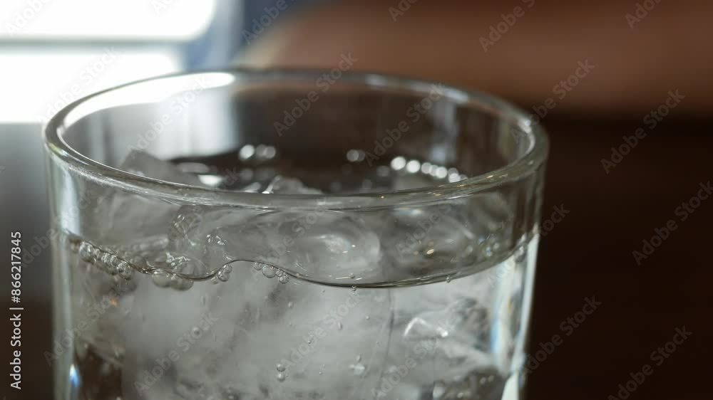Pouring drinking water from plastic bottle over a glass of ice cubes for drinking in restaurant dinner meal time Pouring drinking water from plastic bottle over a glass of ice cubes for drinking in restaurant dinner meal time