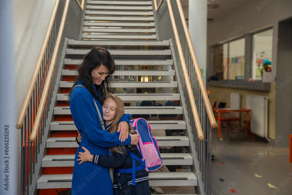 Young brunette in blue dress accompanies her little daughter to school, warm family relations, back to school on a sunny day Young brunette in blue dress accompanies her little daughter to school, warm family relations, back to school on a sunny day