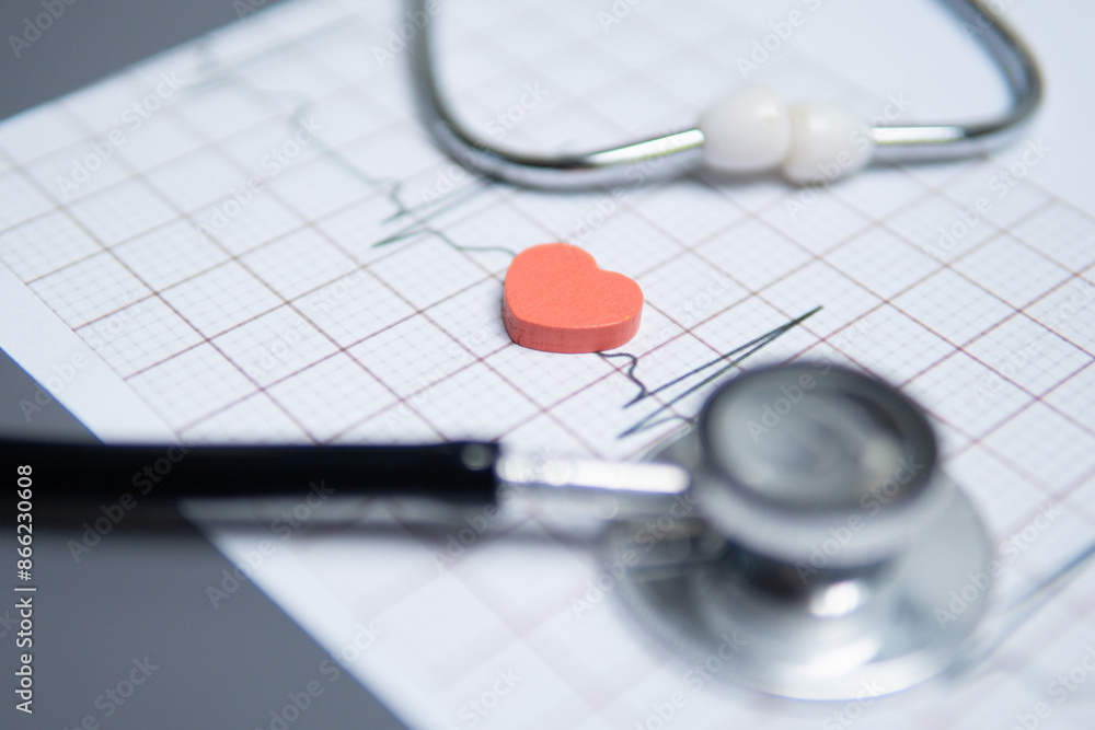 Closeup image of a stethoscope and red heart on a electrocardiogram (ECG) printout. The ECG graph shows a normal sinus rhythm. Healthy heart, wellbeing concept. Closeup image of a stethoscope and red heart on a electrocardiogram (ECG) printout. The ECG graph shows a normal sinus rhythm. Healthy heart, wellbeing concept.