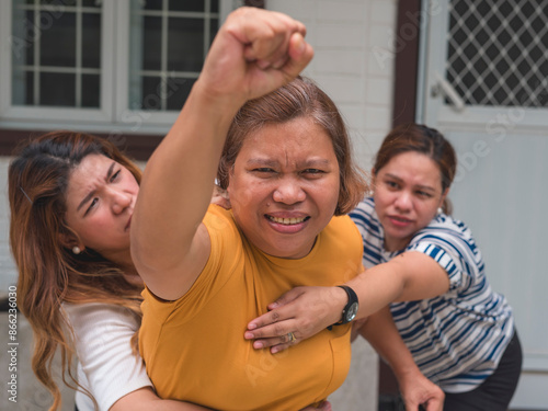 Two concerned women holding back their angry friend from charging towards someone. The angry woman has her fist raised, and the scene exudes tension and emotion.