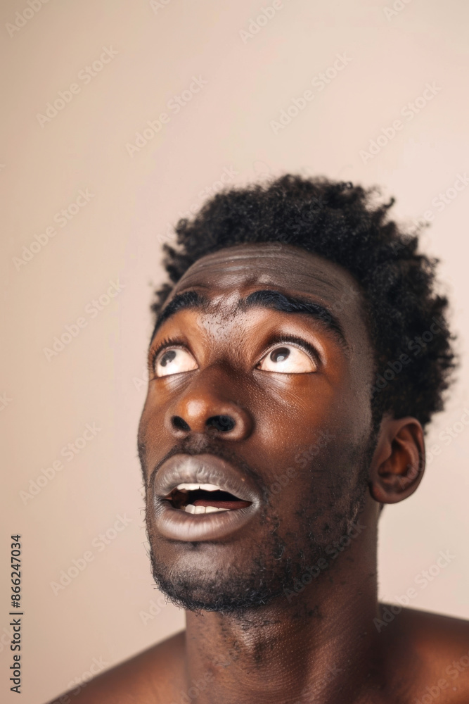 Obraz premium African American man looking up with surprised expression, portrait with neutral background