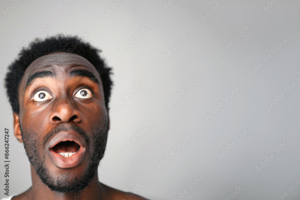African American man with wide-eyed expression, looking up against grey background African American man with wide-eyed expression, looking up against grey background