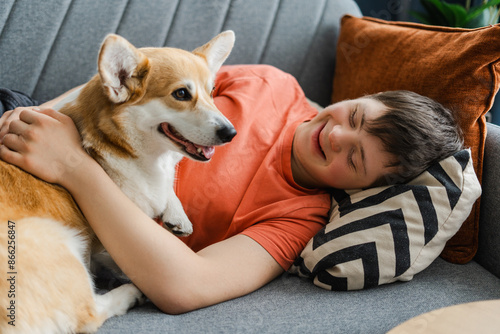 Happy teenager with down syndrome relaxing on sofa at home hugging pet dog photo