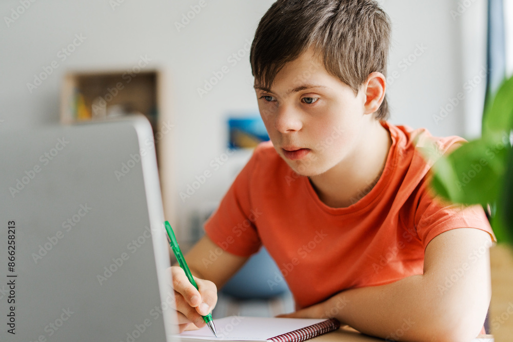 Focused teenager with down syndrome studying online, taking notes Focused teenager with down syndrome studying online, taking notes