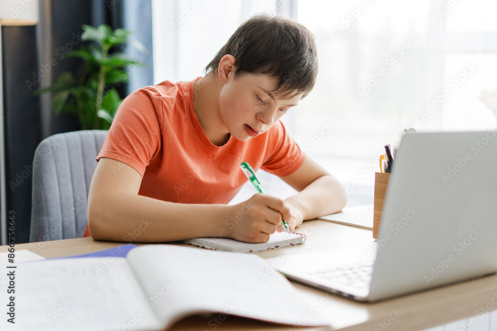 Young student with down syndrome is studying at home using laptop, sitting at home Young student with down syndrome is studying at home using laptop, sitting at home