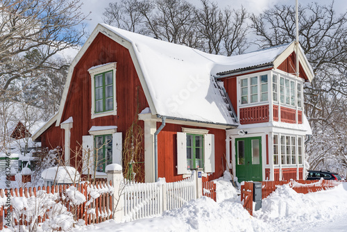Traditional old big red wooden house in winter countryside. Beautiful Swedish cottage or villa with big windows, glazed terrace and balcony. Christmas landscape in northern Europe. Snowy village.
