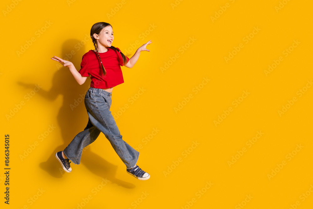 Full size photo of lovely small girl jump run empty space wear t-shirt isolated on yellow color background Full size photo of lovely small girl jump run empty space wear t-shirt isolated on yellow color background