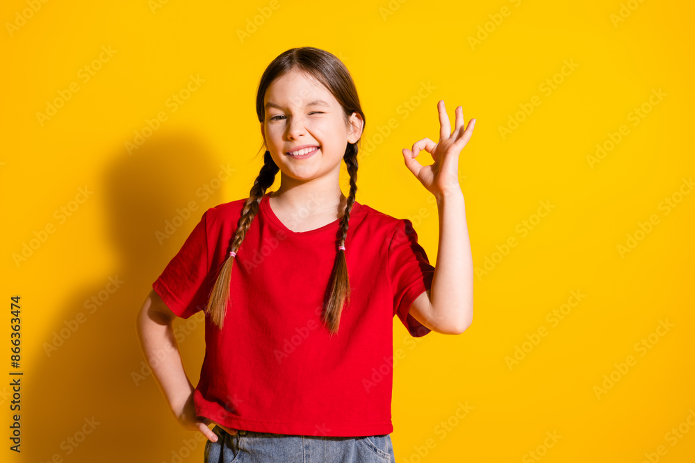 Photo of lovely small girl eye wink show okey symbol wear t-shirt isolated on yellow color background Photo of lovely small girl eye wink show okey symbol wear t-shirt isolated on yellow color background