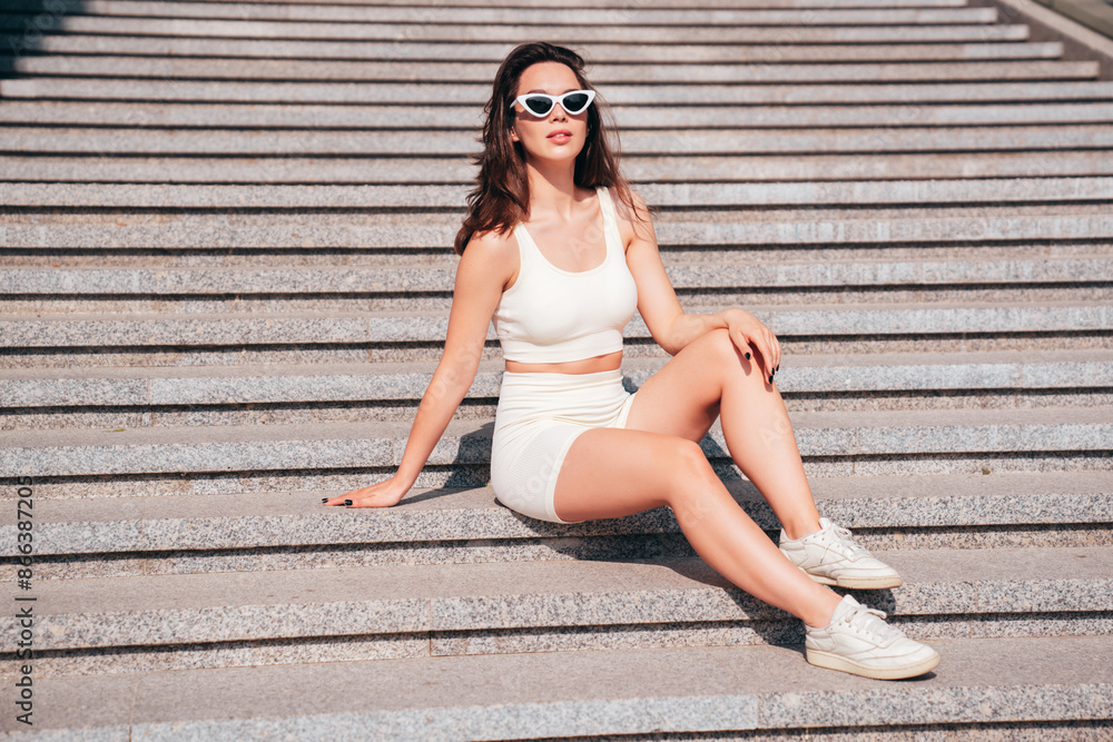 Young beautiful smiling female in trendy summer white cycling shorts and tank top clothes. Sexy carefree woman posing in street. Positive model. Cheerful and happy. Slim and fit body. In sunglasses Young beautiful smiling female in trendy summer white cycling shorts and tank top clothes. Sexy carefree woman posing in street. Positive model. Cheerful and happy. Slim and fit body. In sunglasses