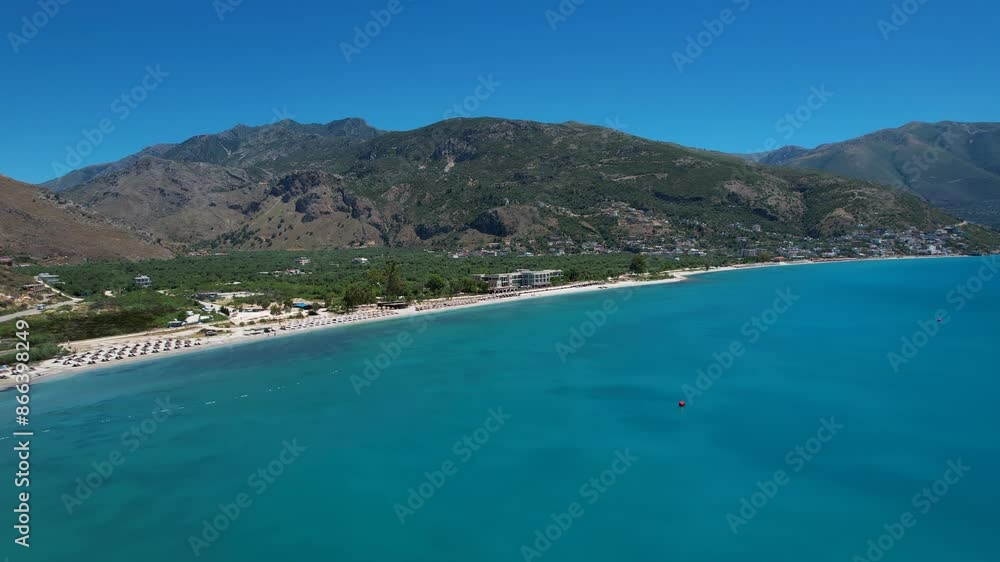 Bay with Azure Seawater on Ionian Coastline of Albania, Calm Beach with White Sand, Green Olive Grove, and Mountains in Background Bay with Azure Seawater on Ionian Coastline of Albania, Calm Beach with White Sand, Green Olive Grove, and Mountains in Background